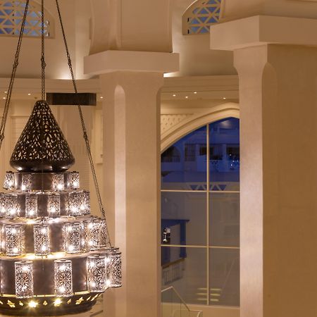 Pickalbatros Palace Sharm - "Aqua Park" Exterior photo The photo shows a beautifully designed chandelier hanging from the ceiling of a spacious interior. The chandelier features a structure with multiple levels and includes ornate patterns, likely made of metal or glass, that diffuse light elegantly. The
