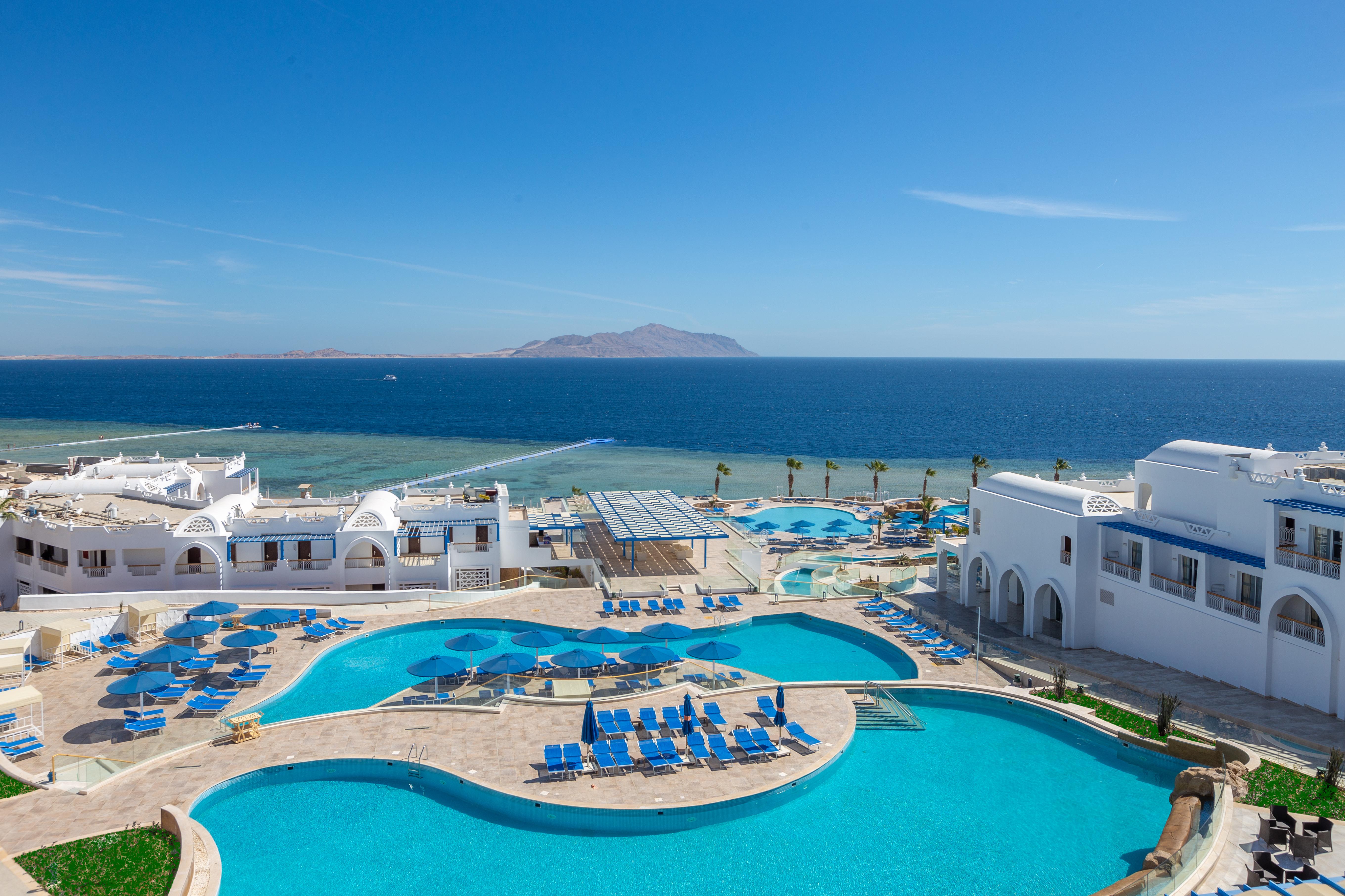 Pickalbatros Palace Sharm - "Aqua Park" Exterior photo The image shows a beautiful seaside resort with multiple swimming pools surrounded by lounge chairs. The pools are designed in various shapes, and the area is adorned with sun umbrellas. In the background, you can see the clear blue ocean and a dista