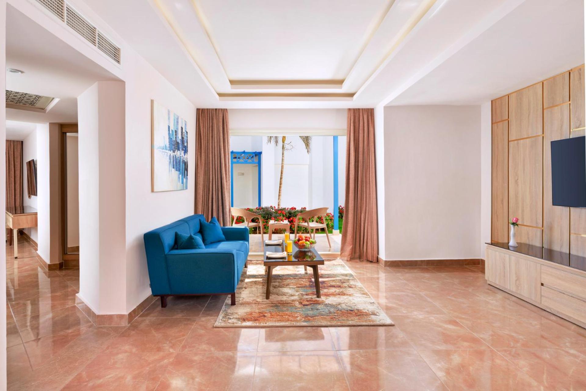 Pickalbatros Palace Sharm - "Aqua Park" Exterior photo The photo shows a modern living room decorated with a bright and inviting style. In the center, there is a cozy blue sofa positioned against a wall. A coffee table sits in front of the sofa, accompanied by a decorative rug underneath. The room featur