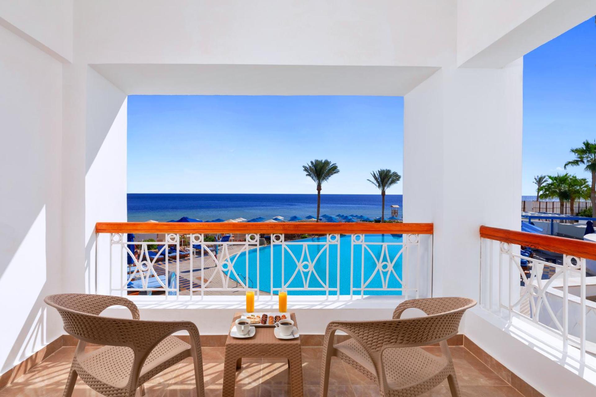Pickalbatros Palace Sharm - "Aqua Park" Exterior photo The photo shows a bright and inviting balcony with two wicker chairs and a small table. On the table, there are two glasses of orange juice and a plate of food. The balcony overlooks a beautiful view of the ocean, with the deep blue water stretching 