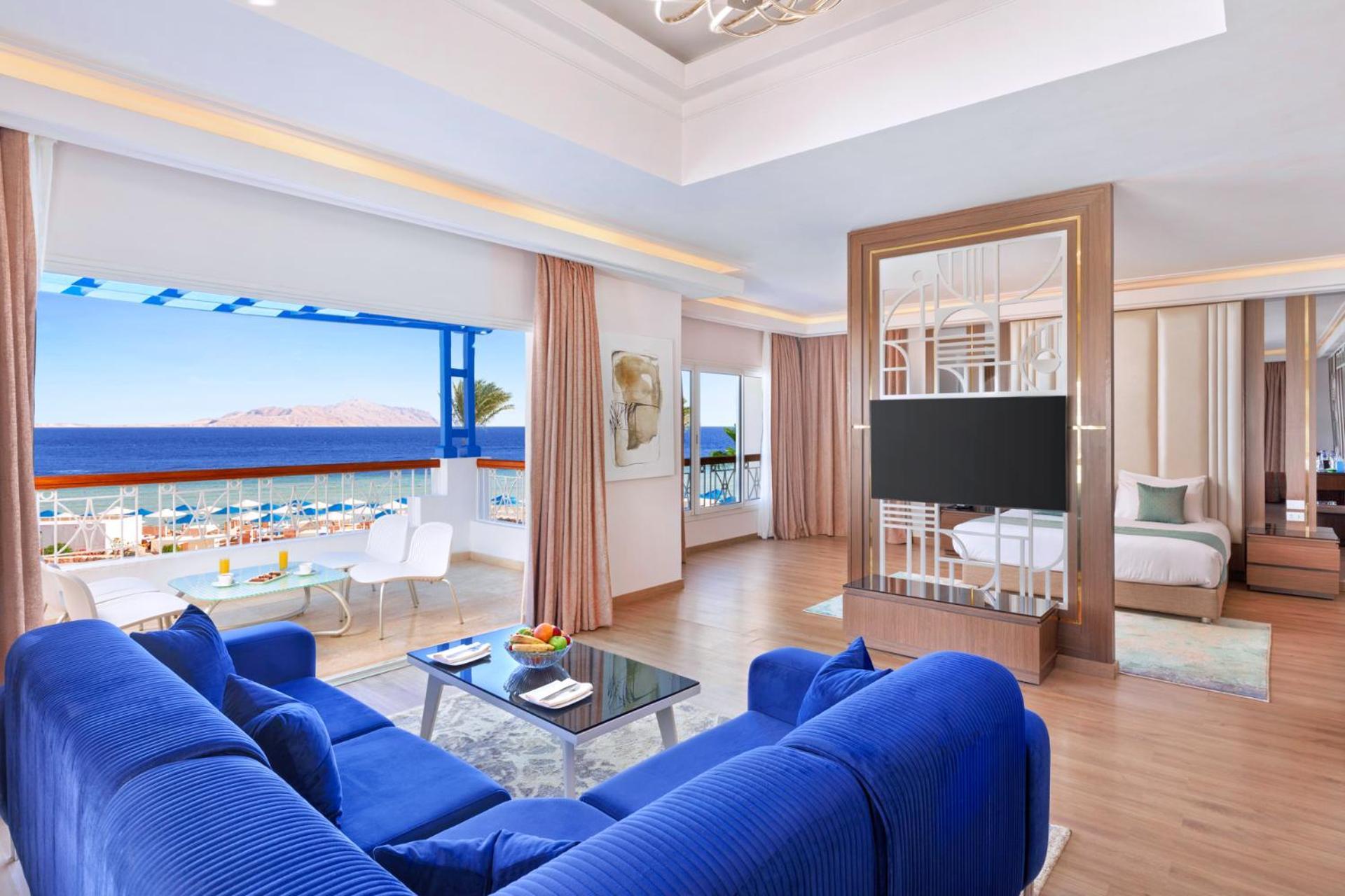 Pickalbatros Palace Sharm - "Aqua Park" Exterior photo The photo shows a well-appointed hotel room or suite featuring a modern and stylish design. There is a spacious living area with a large blue sofa and a glass coffee table in the center. The room is bright, with natural light coming in from large win