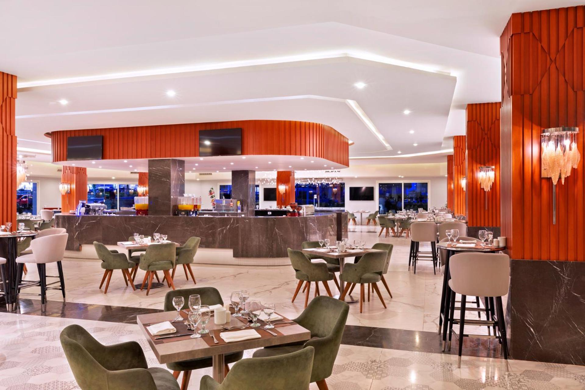Pickalbatros Palace Sharm - "Aqua Park" Exterior photo The photo depicts a modern restaurant interior. The space features a stylish bar area with a curved counter and bright lighting. There are multiple dining tables set with tableware, including plates and glasses. The design includes a mix of seating o